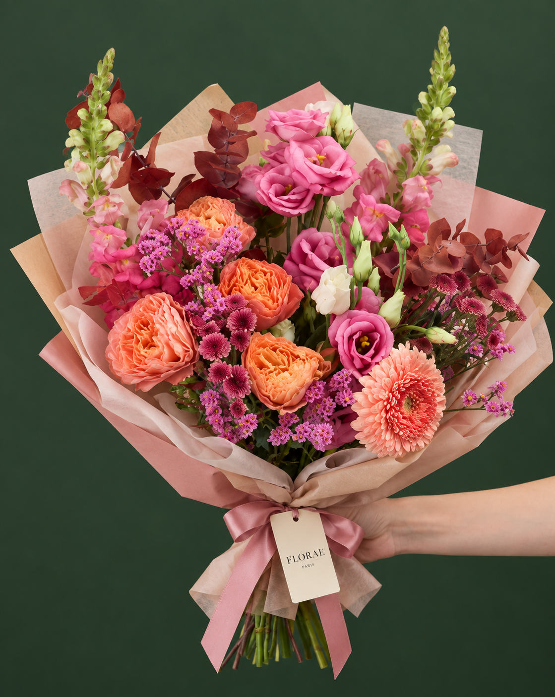 Éclat Corail — Roses corail, lisianthus roses, gerbera pêche, fleurs élancées, petites fleurs mauves et feuillage cuivré. Bouquet Florae sur fond vert.