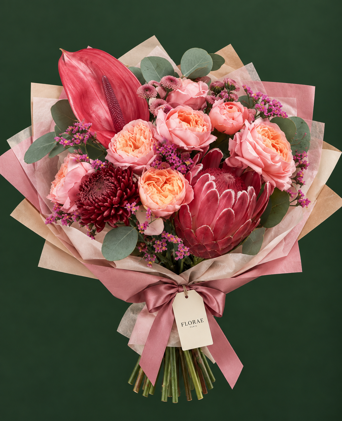 Muse Corail — Protéa, anthurium corail, roses pêche, chrysanthèmes bordeaux, petites fleurs roses et eucalyptus. Bouquet Florae sur fond vert.